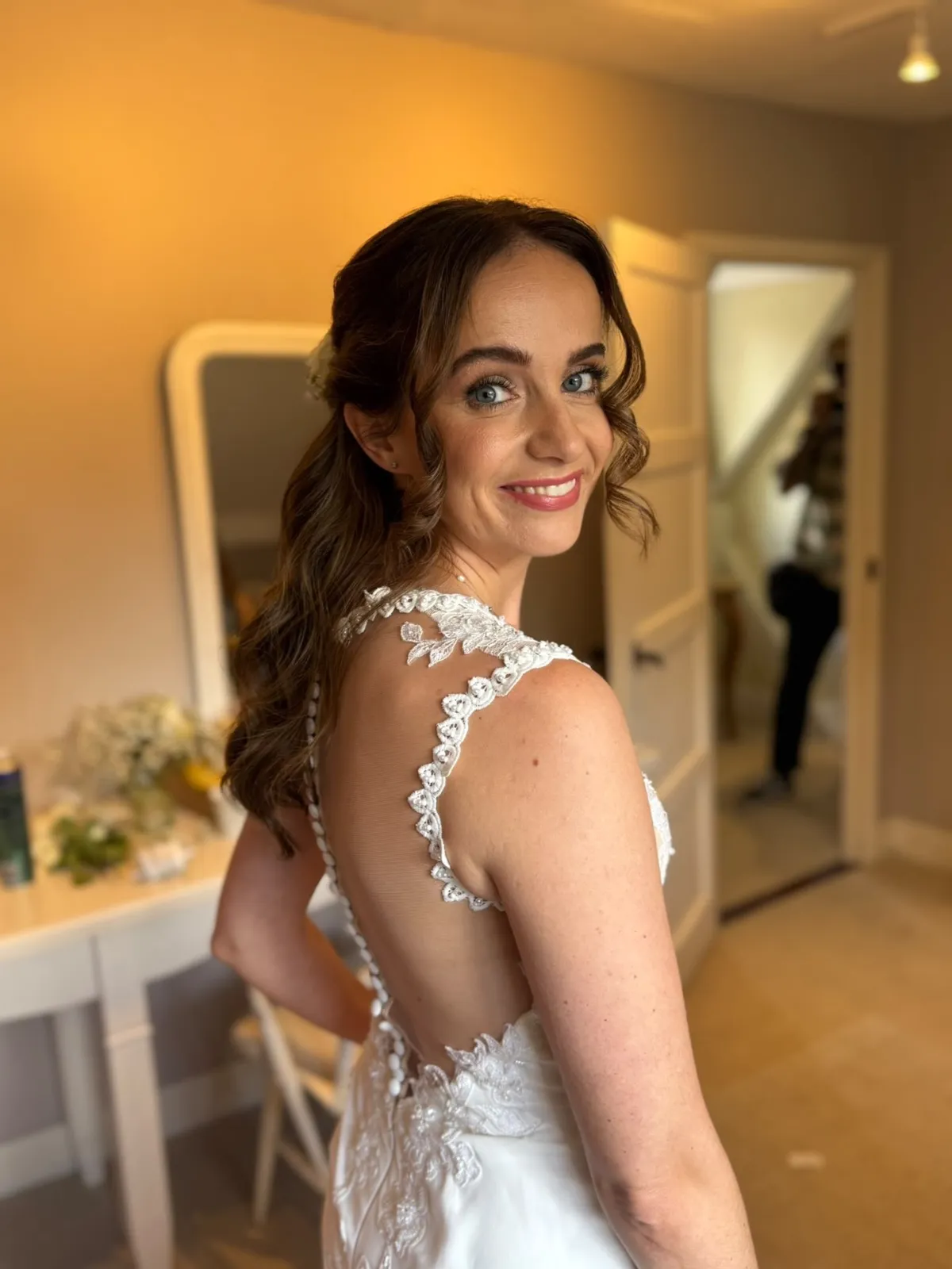 Smiling bride in a lace-back gown with soft half-up waves by Be Bridal
