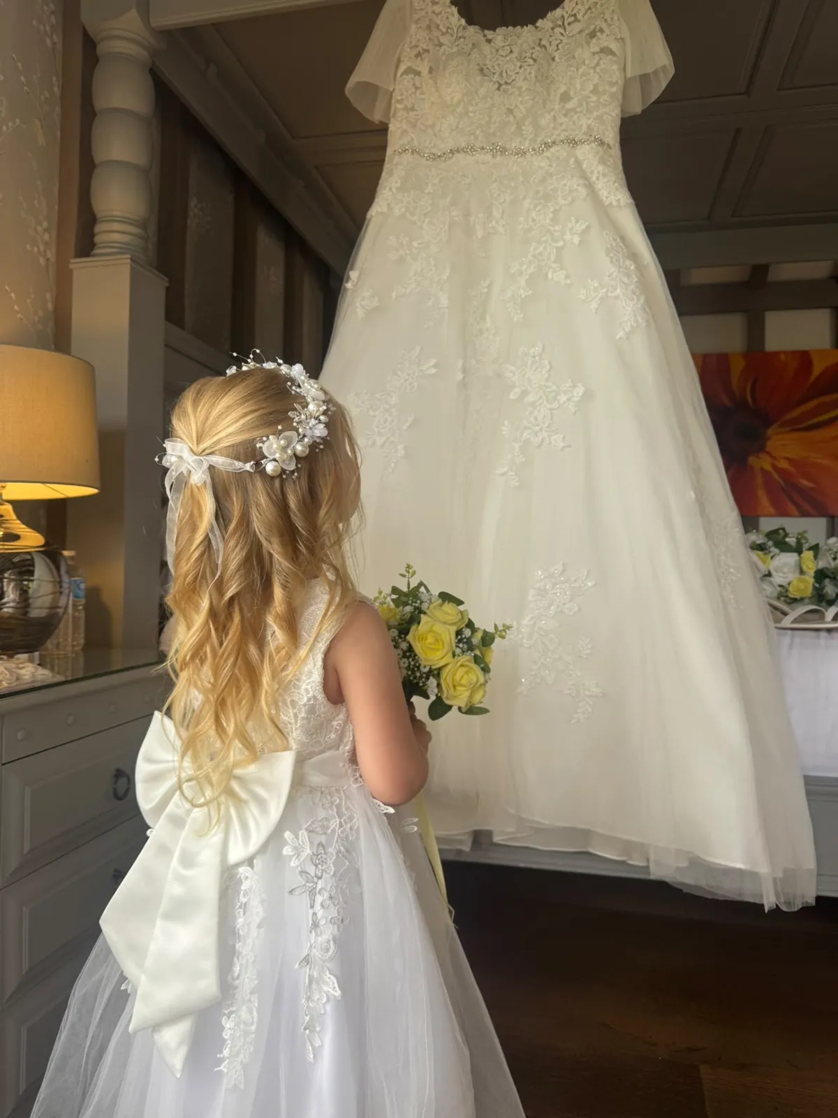 Flower girl with long curls and a pearl halo admiring the wedding dress by Be Bridal