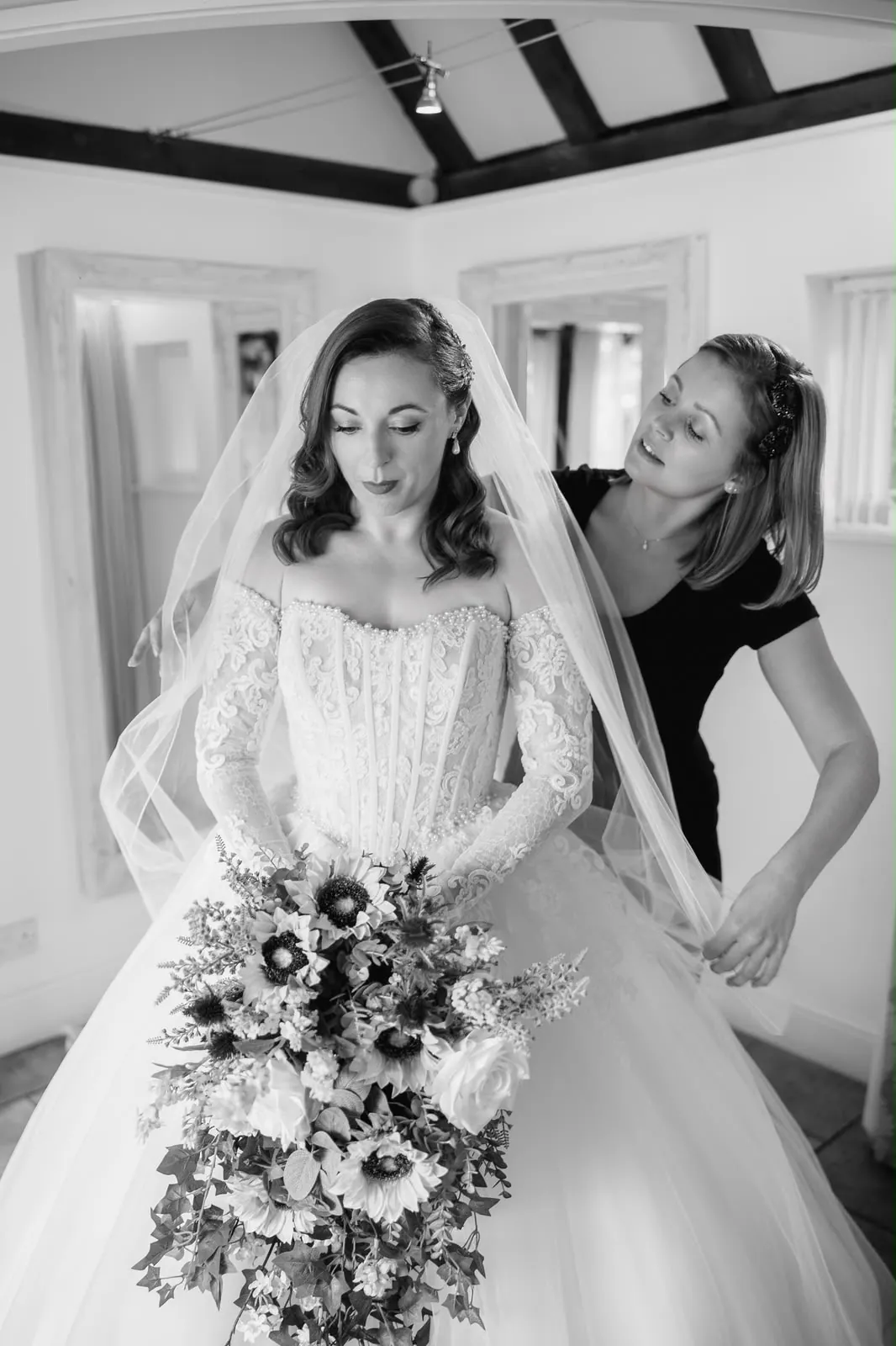 Bride in a lace ballgown having her veil adjusted before the ceremony by Be Bridal