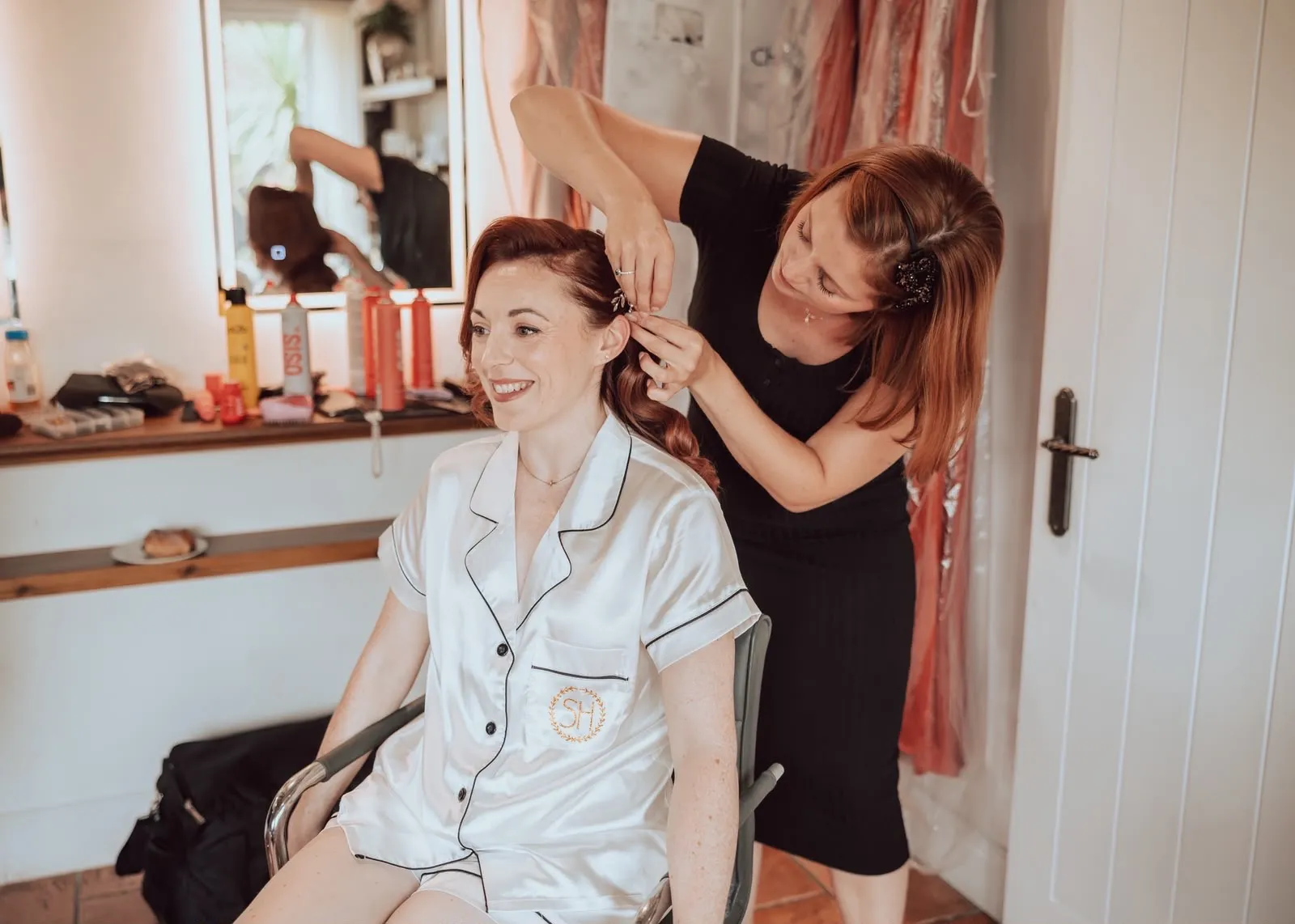 Artist placing a hair vine in a red-haired bride's side-swept waves by Be Bridal