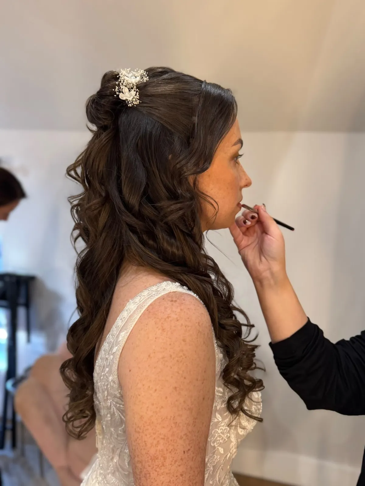 Bride with long half-up curls having her lip colour applied by Be Bridal