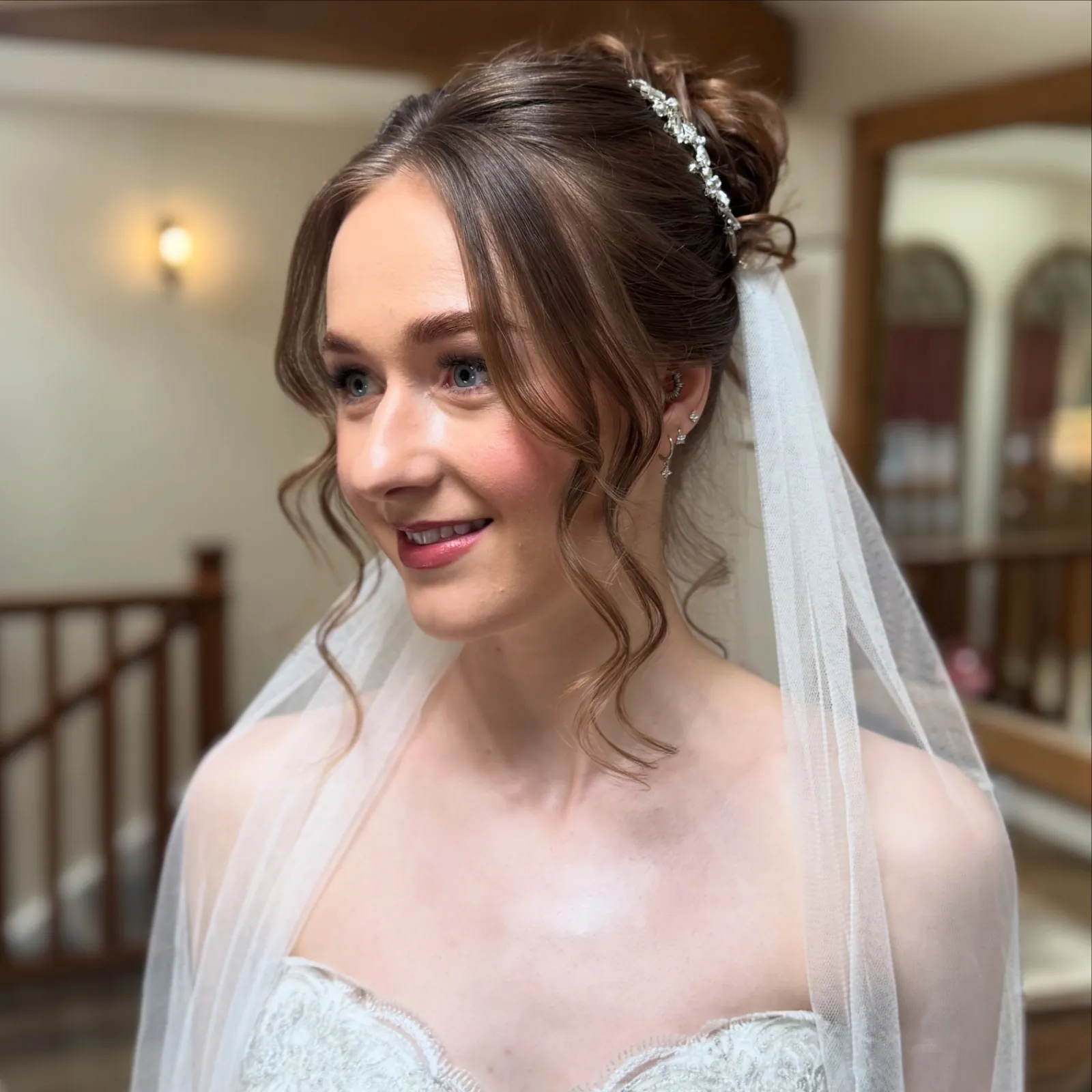 Brunette bride with a high textured bun and crystal hair vine wearing a veil in a timber-beamed suite by Be Bridal