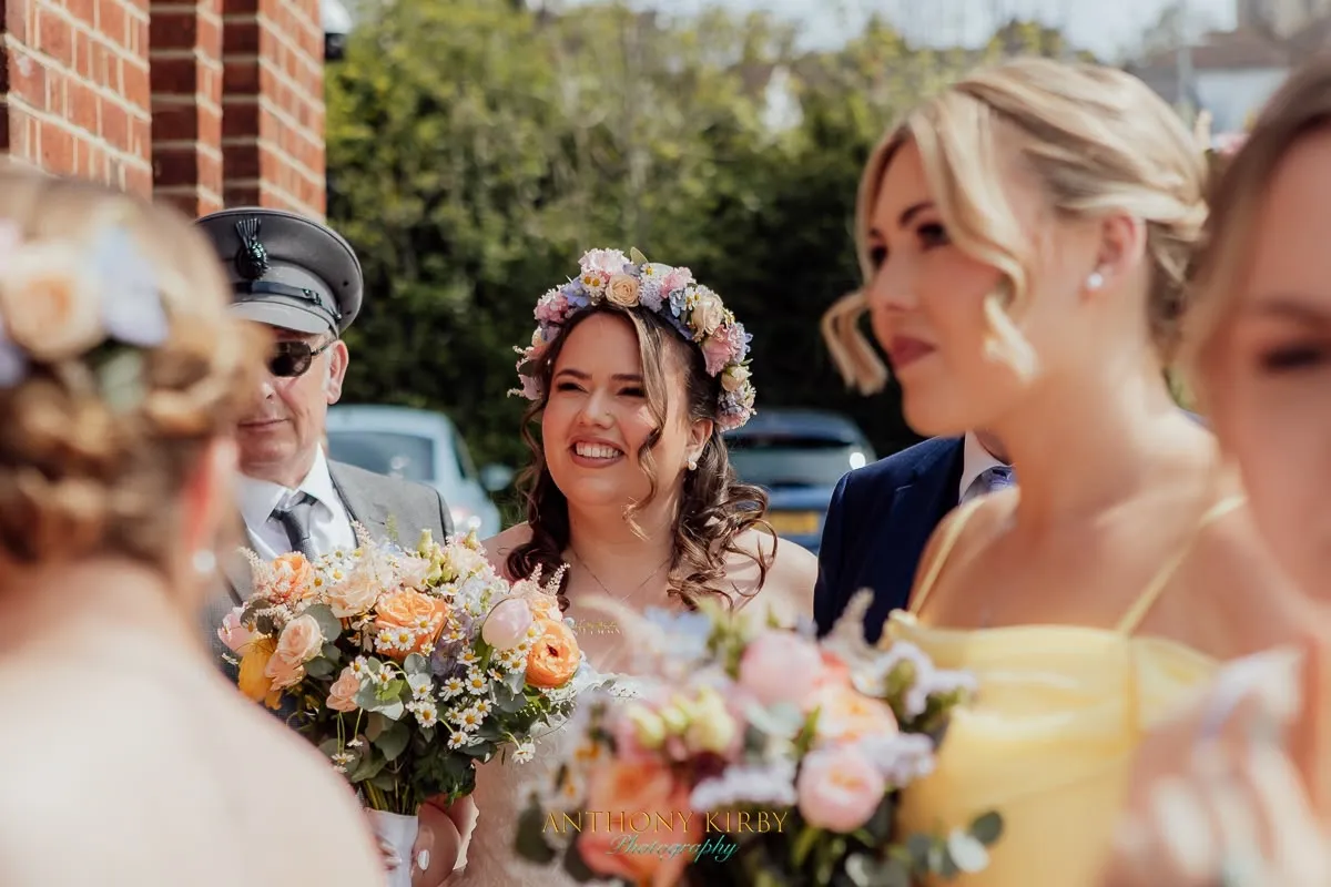 Smiling bride in a floral crown with soft curls arriving with her bridal party by Be Bridal