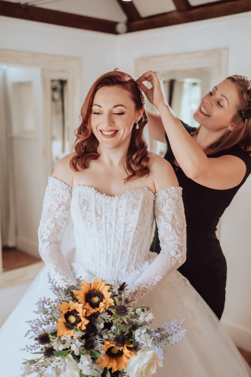 Red-haired bride in a pearl lace gown having her veil placed by Be Bridal