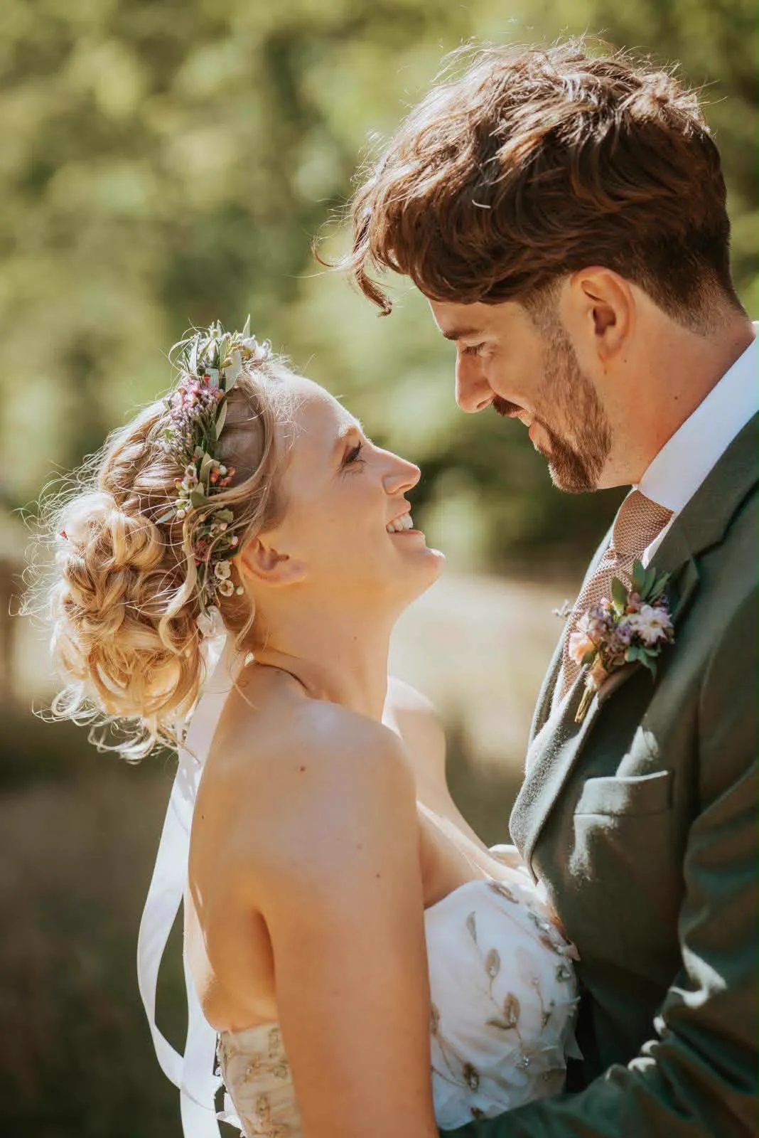 Bride and groom smiling at each other, her floral crown updo in the sunshine by Be Bridal