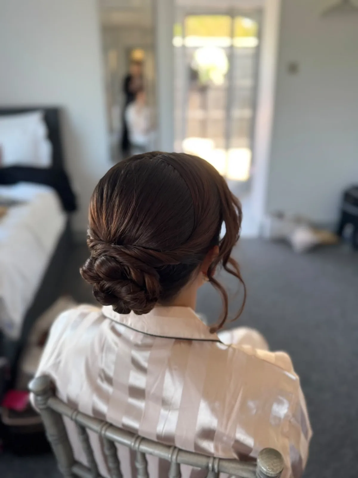 Polished auburn twisted low bun with soft face-framing tendrils by Be Bridal