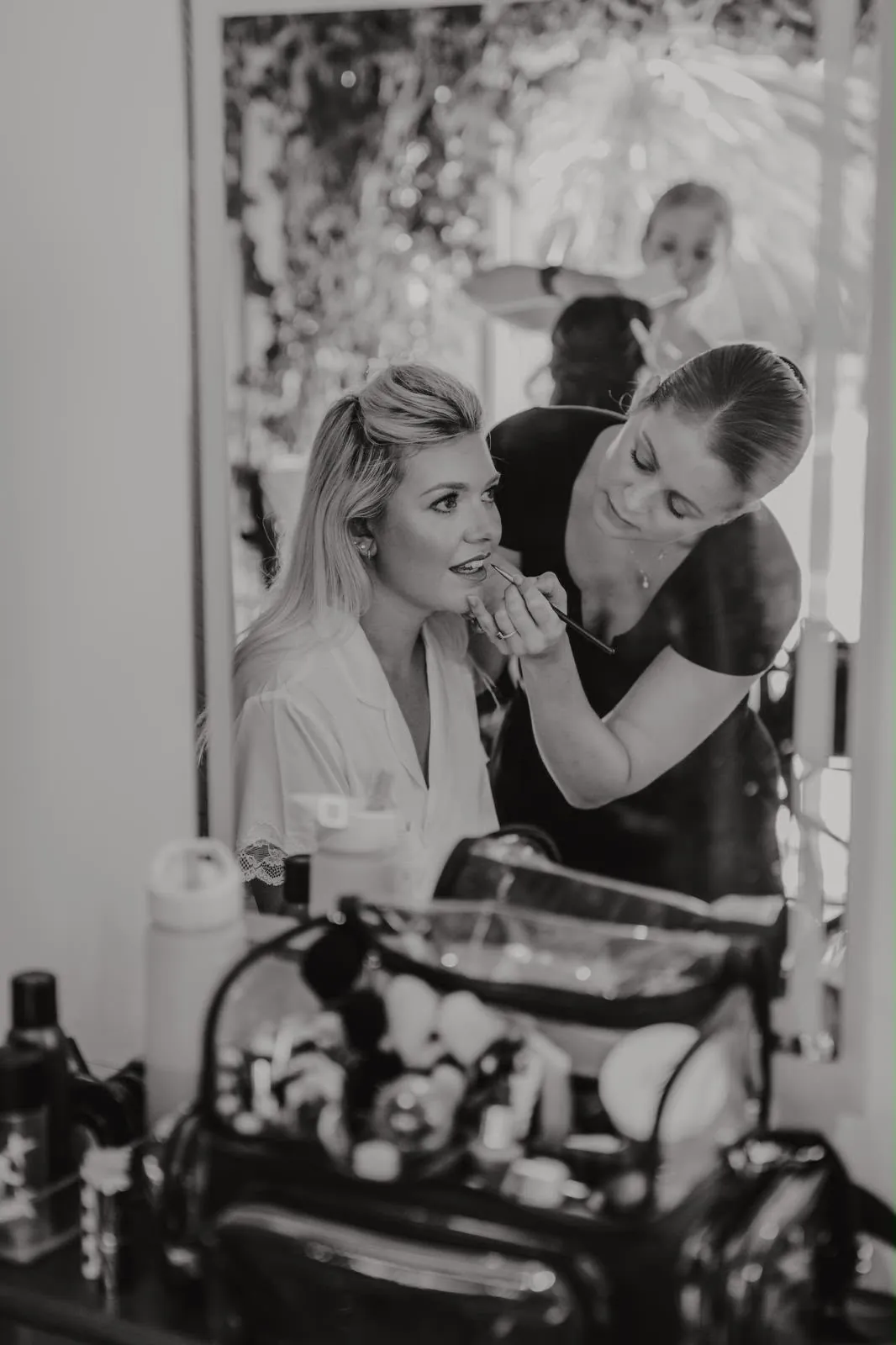 Makeup artist applying a bride's lip colour in the mirror during wedding morning preparation by Be Bridal